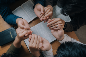 Group of people holding hands over the Bible in prayer for National Day of Prayer. By witsarut/Stock.Adobe.com.