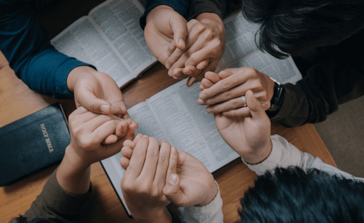 Group of people holding hands over the Bible in prayer for National Day of Prayer. By witsarut/Stock.Adobe.com.