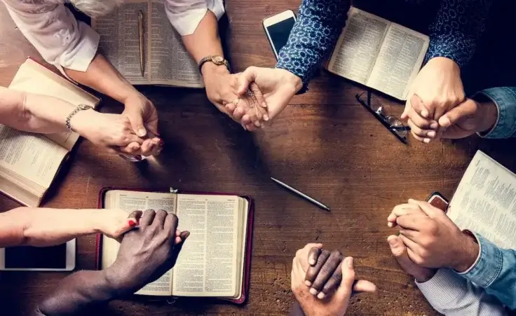 Group of people holding hands praying. By Rawpixel/stock/adobe.com