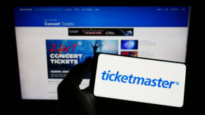 Person holding smartphone with logo of US company Ticketmaster Entertainment Inc. on screen in front of website. By Timon/stock.adobe.com