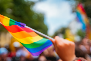 Hand holding a LGBTQ flag at pride festival. By teksomolika/stock.adobe.com.