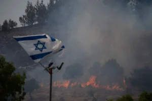 An Israeli flag flutters next to a fire burning in an area near the border with Lebanon, northern Israel in Safed, Wednesday, June 12, 2024. Scores of rockets were fired from Lebanon toward northern Israel on Wednesday morning, hours after Israeli airstrikes killed four officials from the militant Hezbollah group including a senior military commander. (AP Photo/Leo Correa)