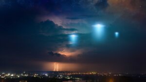 Extraterrestrial aliens spaceship fly above small town, UFO with blue spotlights in dark stormy sky. By IgorZh/stock/adobe.com
