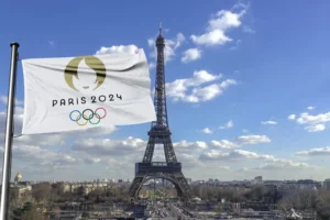 The Eiffel tower with the Olympic flag flying in the foreground that reads "Paris 2024". By Iliya Mitskavets/Stock.Adobe.com