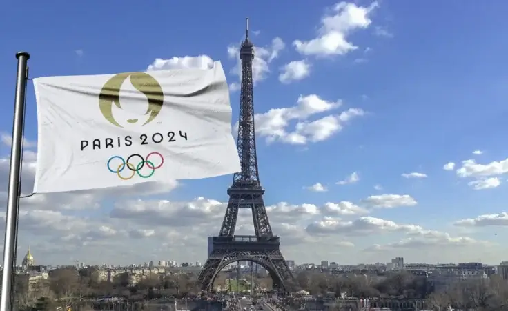 The Eiffel tower with the Olympic flag flying in the foreground that reads "Paris 2024". By Iliya Mitskavets/Stock.Adobe.com