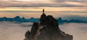 Epic adventure composite of a hiker on top of a rocky mountain to illustrate man striving to achieve perfectionism. By edb3_16/stock.adobe.com