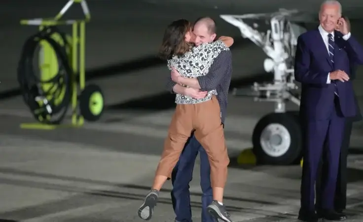 Reporter Evan Gershkovich hugs his mother, Ella Milman, as President Joe Biden, right, looks on at Andrews Air Force Base, Md., following their release as part of a 24-person prisoner swap between Russia and the United States, Thursday, Aug. 1, 2024. (AP Photo/Manuel Balce Ceneta)
