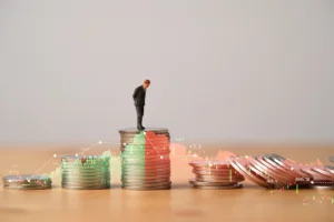 Miniature figure standing on coins stacking with increasing and decreasing stock market graph. By Dilok/stock.adobe.com. Recession