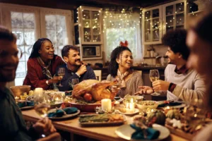 Friends sitting around a thanksgiving dinner table. By Drazen/stock.adobe.com.