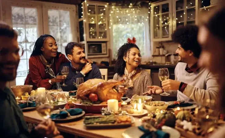 Friends sitting around a thanksgiving dinner table. By Drazen/stock.adobe.com.