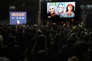 Relatives and friends of people killed and abducted by Hamas and taken into Gaza, react while photographs of the kidnapped women awaiting release Romi Gonen, Doron Steinbrecher and Emily Damari appear on the screen in Tel Aviv, Israel on Sunday, Jan. 19, 2025. (AP Photo/Oded Balilty)