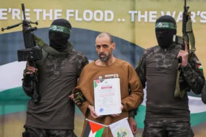 Israeli captive, Eli Sharabi, who has been held hostage by Hamas in Gaza since October 7, 2023, stands on a stage escorted by Hamas fighters before being handed over to the Red Cross in Deir al-Balah, central Gaza Strip, Saturday Feb. 8, 2025. (AP Photo/Abdel Kareem Hana) Gaza hostages