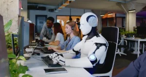 Robot working at computer among people to illustrate the future of AI robots. By ihorvsn/stock.adobe.com