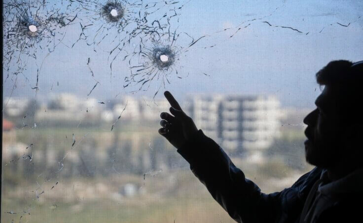 A nurse points to bullet holes in a window following the recent wave of violence between Syrian security forces and gunmen loyal to former President Bashar Assad, as well as subsequent sectarian attacks, at a hospital in the town of Jableh, in Syria's coastal region, on Monday, March 10, 2025. (AP Photo/Omar Albam)