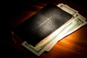 Bibel mit Geldscheinen im Spotlight By Angela Rohde/stock.adobe.com