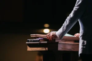 Pastor with hands on pulpit to represent the idea that pastors should be pillars in their communities rather than celebrities with a platform. By Chris/stock.adobe.com