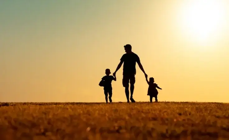 Silhouette of father and children holding hands walking outdoors in the park. By kieferpix/stock.adobe.com