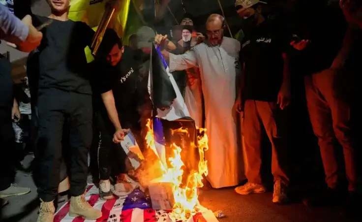 Protesters burning the Israeli and U.S. flags during a protest against Israeli attacks on multiple cities across Iran at a bridge leading to the fortified Green Zone where the U.S. Embassy is located in Baghdad, Iraq, Monday, June 16, 2025. (AP Photo/Hadi Mizban)