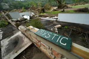 A Camp Mystic sign is seen near the entrance to the establishment along the banks of the Guadalupe River after a flash flood swept through the area in Hunt, Texas, Saturday, July 5, 2025. (AP Photo/Julio Cortez)