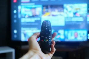 A hand holding a TV remote with streaming platforms displayed in the background. By Mihail/stock.adobe.com. Stephen Colbert