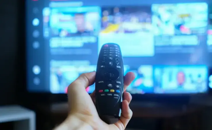 A hand holding a TV remote with streaming platforms displayed in the background. By Mihail/stock.adobe.com. Stephen Colbert