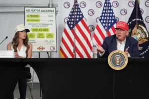 President Donald Trump speaks during a roundtable at "Alligator Alcatraz," a new migrant detention facility at Dade-Collier Training and Transition facility, Tuesday, July 1, 2025, in Ochopee, Fla., as Homeland Security Secretary Kristi Noem, looks on. (AP Photo/Evan Vucci)