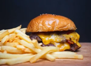 Close-up of juicy grilled cheeseburger and golden french fries on rustic surface. By meeboonstudio/stock.adobe.com