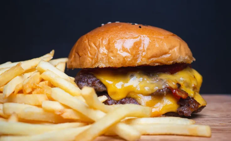 Close-up of juicy grilled cheeseburger and golden french fries on rustic surface. By meeboonstudio/stock.adobe.com
