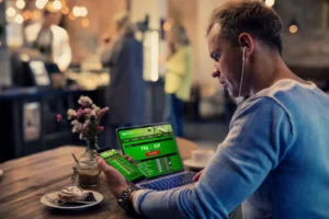 Man using online sports betting services on phone and laptop By Kaspars Grinvalds/stock.adobe.com