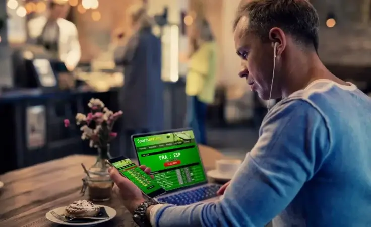 Man using online sports betting services on phone and laptop By Kaspars Grinvalds/stock.adobe.com