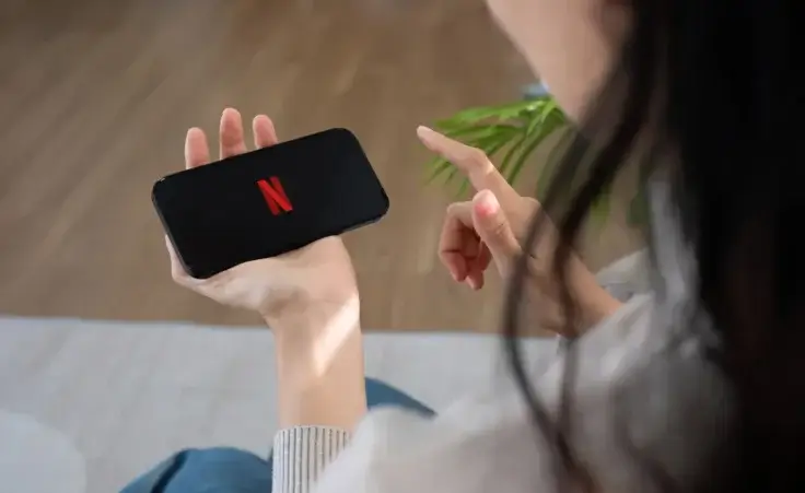 Woman loading the Netflix streaming app on a cell phone. By wichayada/stock.adobe.com.
