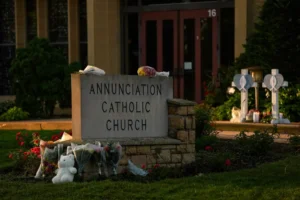Crosses, flowers and other mementos were places by the sign at Annunciation Catholic Church at a memorial after Wednesday's shooting at the school, Thursday, Aug. 28, 2025, in Minneapolis. (AP Photo/Abbie Parr)