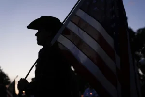 Koda holds an American flag as attendees pay their respects during a vigil for Charlie Kirk on Friday, Sept. 12, 2025, in Provo, Utah. (AP Photo/Lindsey Wasson) Turning Point