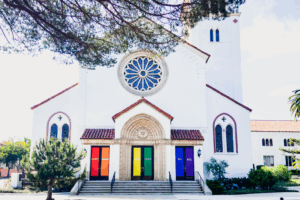 "God's Doors Are Open To All," a sign displayed on the doors of a church in support of pride month. By glimmersDarkly/stock.adobe.com. LGBTQ storybook bible social justice