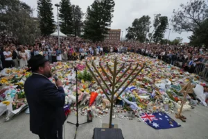 Rabbi Motti Feldman speaks at a menorah lighting ceremony at a floral memorial for victims of Sunday's shooting, at the Bondi Pavilion at Bondi Beach on Tuesday, Dec. 16, 2025, in Sydney, Australia. (AP Photo/Mark Baker)