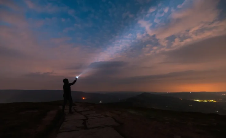 Silhouette of a woman with flashlight under the night sky with dawn on the horizon. By william87/stock.adobe.com. how to find hope in the new year