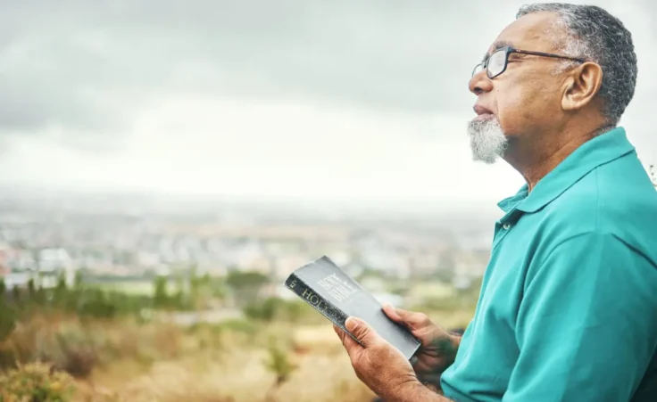 Bible, praying or senior man in nature for praise, hope or Christian religion with holy mindfulness. Prayer moment, calm pastor or mature person in worship with faith, spiritual and sky mockup By aLListar/peopleimages.com/stock.adobe.com