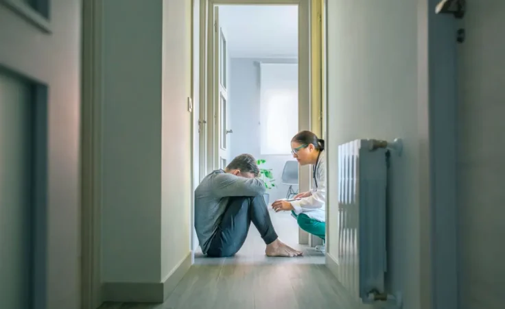 Female psychiatrist talking to male patient with mental disorder and suicidal thoughts sitting on the room floor of hallway By David Pereiras/stock.adobe.com
