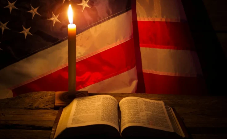 Burning candle and open book. America's flag behind burning candle. Night at old church. Never lose faith. By DenisProduction.com/stock.adobe.com