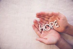 Wooden word "HOPE" on praying hands in a gratitude, faith concept. By SewcreamStudio/stock.adobe.com.