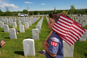 Christian Marquand, 6, from Cub Scout Pack 620 in Highlands Ranch, Colo., carries flags during the annual placing of U.S. flags at the gravesites of military veterans at Fort Logan National Cemetery in southwest Denver, on Sunday, May 24, 2026, to mark Memorial Day. (AP Photo/David Zalubowski)