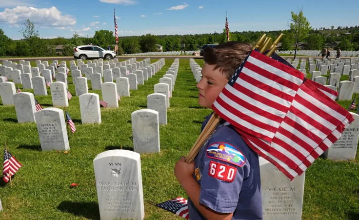 Christian Marquand, 6, from Cub Scout Pack 620 in Highlands Ranch, Colo., carries flags during the annual placing of U.S. flags at the gravesites of military veterans at Fort Logan National Cemetery in southwest Denver, on Sunday, May 24, 2026, to mark Memorial Day. (AP Photo/David Zalubowski)