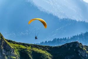 A yellow paraglider flies over a mountain slope. By DmitriiPotashkin/stock.adobe.com. plane