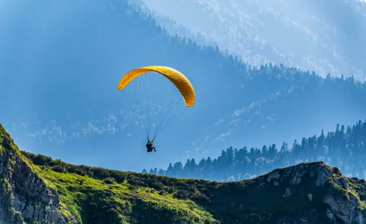 A yellow paraglider flies over a mountain slope. By DmitriiPotashkin/stock.adobe.com. plane