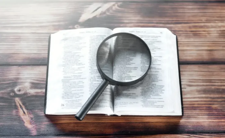 Open bible on a wooden table. Magnifier by amdre100/stock.adobe.com